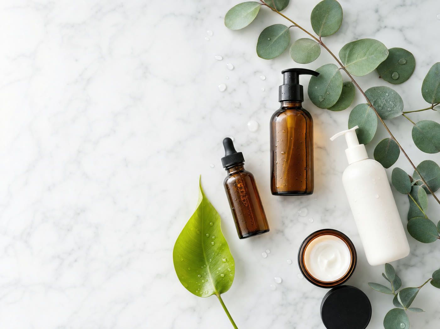 Amber and white botanical product bottles with eucalyptus and a green leaf on marble